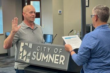 A man stands behind a City of Sumner podium with his right hand raised, being sworn in by a woman holding a document.