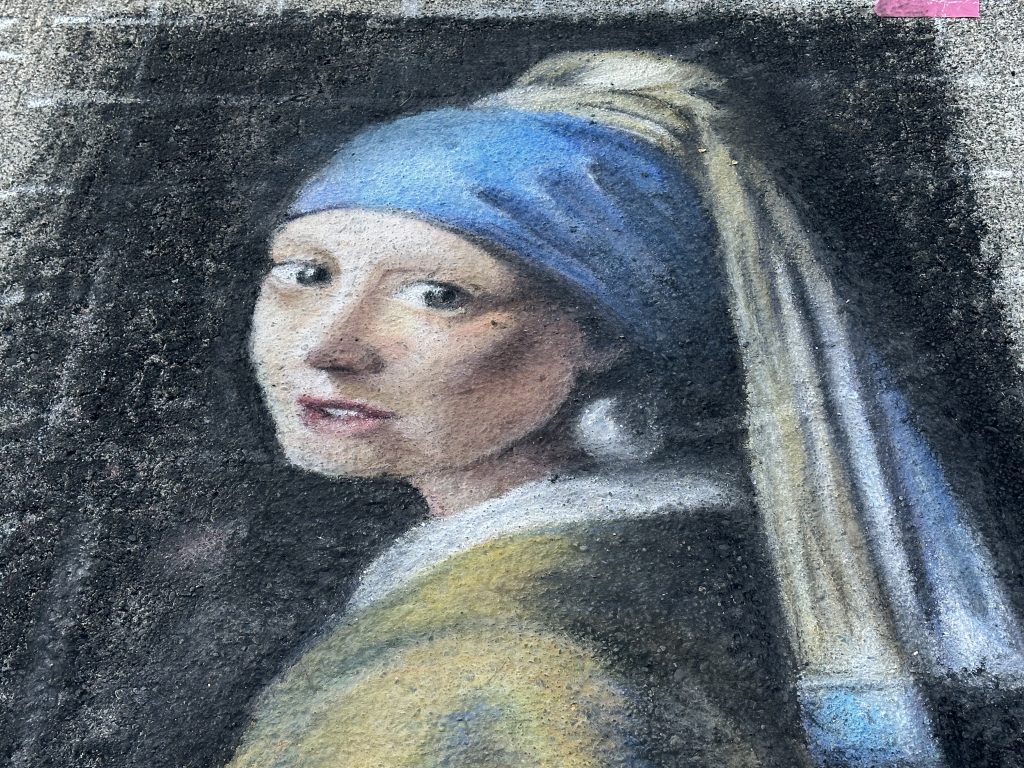 Street art reproduction of Vermeer's Girl with a Pearl Earring rendered in chalk on asphalt pavement.