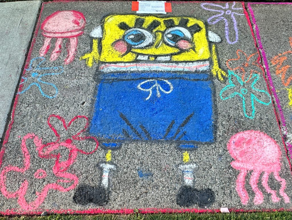 Chalk sidewalk drawing of SpongeBob SquarePants with pink jellyfish and colorful flowers on a gray pavement.