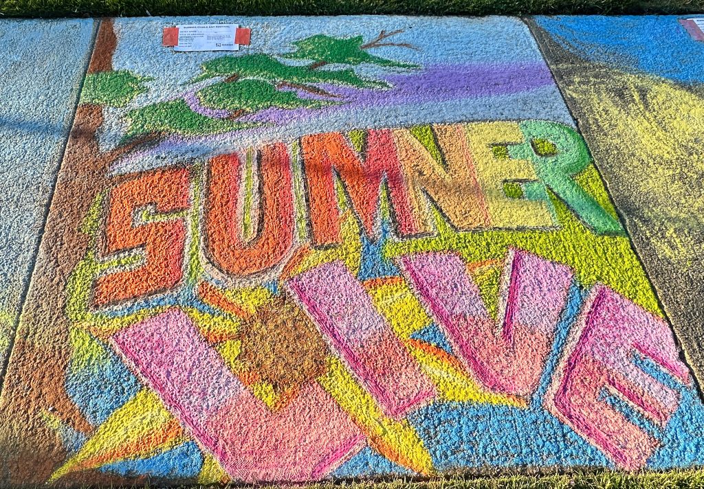 Chalk art on a sidewalk displaying the words 'SUMMER LIVE' in vibrant, blocky 3D lettering against a nature-themed background.